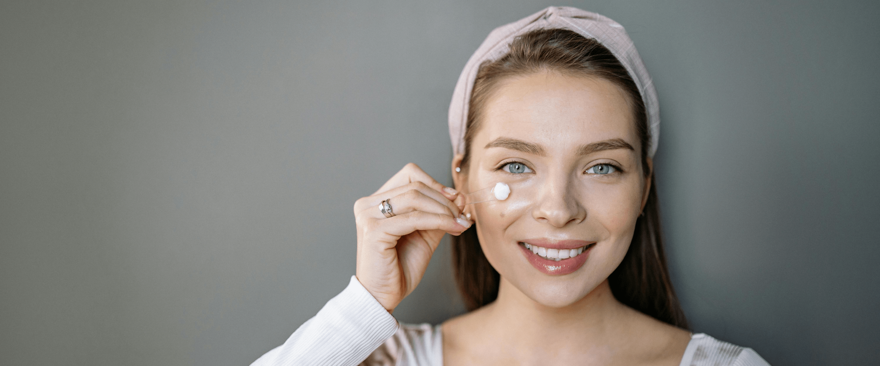 Woman applying oil to her face with a neutral background